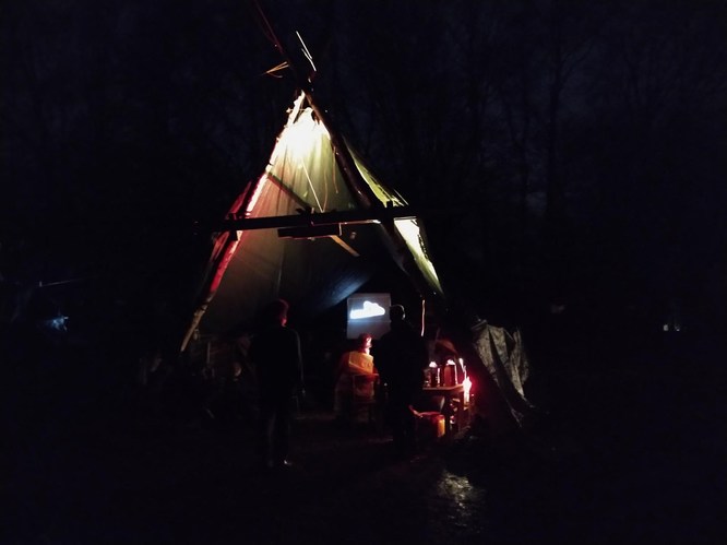 Dark selfmade Tent in the night, some people, some electric light. Background: Trees