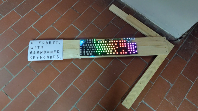 paper showing: a forest. with abandoned keayboards, on a wooden arrow. there is also an mainboard of a gaming keyboard showing some colorful light.